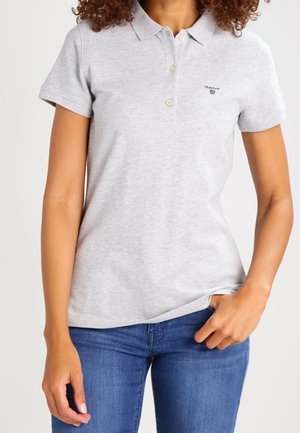 Grijze katoenen polo met een kraag, drie knopen en een klein geborduurd logo op de linkerborst. Gecombineerd met blauwe jeans.
