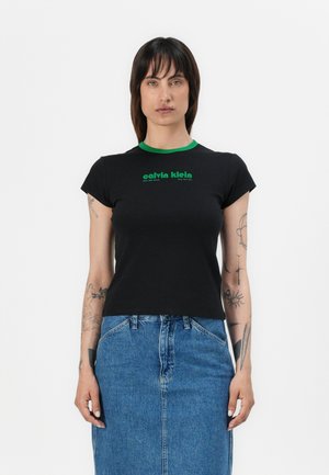 T-shirt noir à manches courtes avec un col rond vert. Présente un logo vert "calvin klein" imprimé sur la poitrine. Matière en coton.