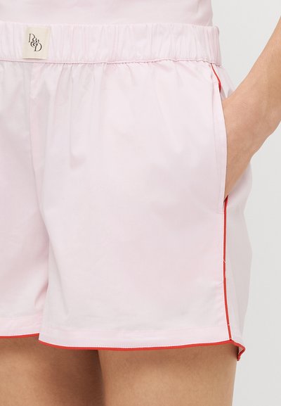 Shorts roses légers en tissu, dotés d'une taille élastique, de poches latérales et d'un liseré rouge contrastant le long des bords.