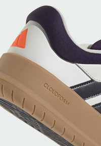 Baskets blanches et bleu marine avec une tige texturée, un col violet rembourré et une semelle extérieure en caoutchouc beige. Présente l'inscription « CLOUDFOAM » embossée sur le côté.