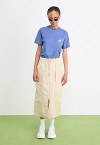 Tricou albastre deschis cu un buzunar pe piept, asociat cu o fustă midi bej cu un fermoar frontal și două buzunare laterale. Adidași albi completează ținuta.