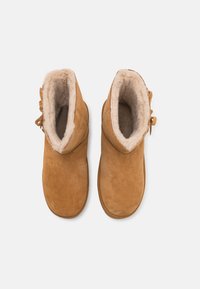 Bruine suede enkellaarsjes met zachte beige nepbont voering, ronde neus, zij-lace detail en een gladde textuur.