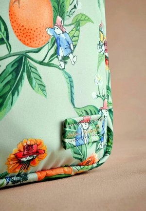 Zaļš auduma soma ar detalizētām ilustrācijām par Paddington lāci starp ziediem un lapām, ar zīmola etiķeti, kas iešūta sānu pusē.