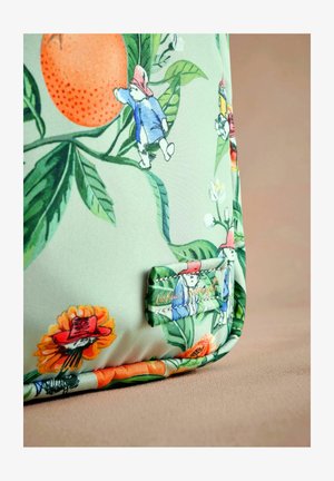 Borsa di stoffa verde con illustrazioni dettagliate di Paddington Bear tra fiori e foglie, con un'etichetta di marca cucita di lato.