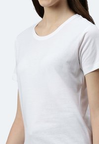 Weißes Baumwoll-T-Shirt mit kurzen Ärmeln, rundem Ausschnitt und glatter Textur. Der Stoff wirkt weich und leicht.