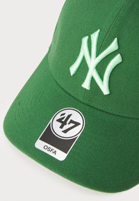 Grøn baseball cap med hvidt broderet "NY" logo, buet skygge, tekstureret stof, og et rundt mærke med nummeret "47" og "OSFA."
