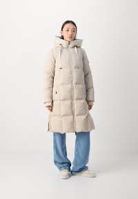 Beige pufferjas met een capuchon, voorzien van een ritssluiting en zijzakken. Soepele stof met een gestikt patroon, lengte tot de knie.