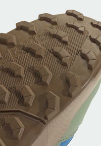 Καφέ λάστιχο σόλα παπουτσιού με υφή επιφάνειας, που διαθέτει γωνιώδεις προεξοχές για κράτημα και συνδυασμό σκούρου καφέ και ανοιχτού πράσινου αποχρώσεων.