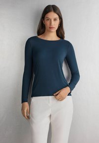 Marineblaues Langarmoberteil aus einem glatten, enganliegenden Stoff; mit einem runden Ausschnitt und dezentem Glanz, kombiniert mit weißen Hosen.