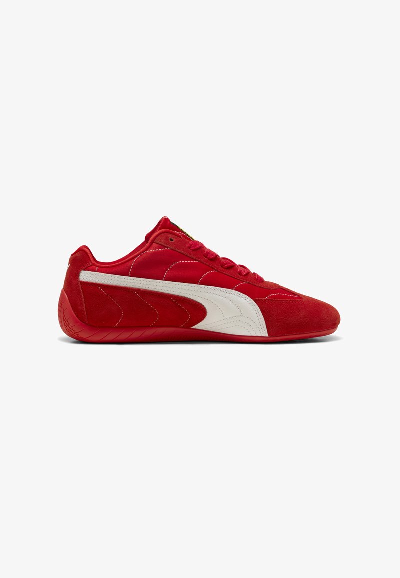 Sneaker rossa a taglio basso con striscia laterale bianca, tomaia in suede e tessuto, e suola in gomma rossa, mostrata in profilo laterale su sfondo bianco.