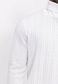 Pull en cachemire blanc avec un col roulé présentant un motif en diamant texturé. Le matériau semble léger et aéré, idéal pour le superposition.