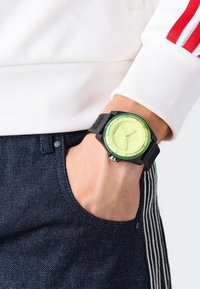 Mustmust musta suur lime roheline nägu, millel on kolm käsi ja tekstuuriga must rihm. Kannab kät, mis on tasku kõrval.