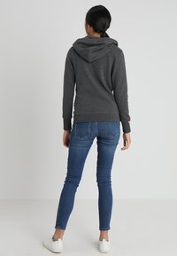 Sweat-shirt à capuche gris avec une texture douce, doté d'une poche kangourou et de poignets côtelés, associé à un jean skinny bleu et des baskets blanches.