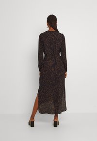 Dlouhé rukávy, tmavé šaty s leopardím vzorem, páskem v pase, bočními rozparky a splývavou tkaninou. Silné boty na blokovém podpatku.