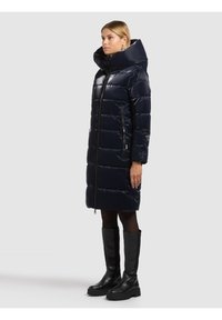 Duga tamnoplava jakna-puhovka s visokim ovratnikom, patentnim zatvaračem sprijeda i dva bočna džepa. Materijal ima sjajni završetak i prošiveni dizajn.