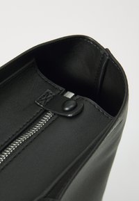 Borsa a mano in pelle nera con chiusura a zip, tirazip in argento e texture interna visibile. Bordo superiore arrotondato e finitura liscia.