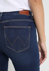 Mörkblå denimjeans med en distinkt bakfickdesign som har ett chevronstickningsmönster. Läderpatch med varumärke vid midjan.