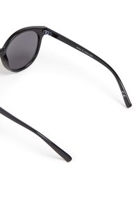 Pyöreät mustat aurinkolasit tummanharmailla linsseillä, valmistettu muovista. Ohuet kehykset, sileä pinta ja hillitty brändäys yhdessä sankassa.