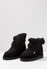 Bottines noires en daim avec une tige texturée et moelleuse, dotées d'un revers en fausse fourrure et d'un design classique à lacets avec œillets métalliques.