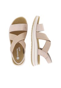 Beige cross-strap sandals with a soft suede-like texture, cushioned footbed, and a white rubber sole with grooves for grip.