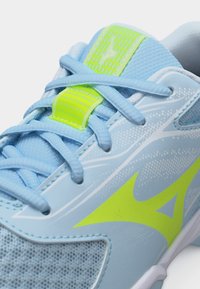 Αθλητικό παπούτσι ανοιχτού μπλε χρώματος με λογότυπο και γλωσσάκι σε νέον κίτρινο, με μπλε κορδόνια που διασταυρώνονται και διχτυωτό ύφασμα κοντά στα δάχτυλα.