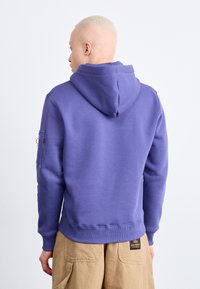 Lila kapucnis pulóver bordázott mandzsettákkal és derékpánttal, oldalzsebbel. Puha, texturált anyagból készült.