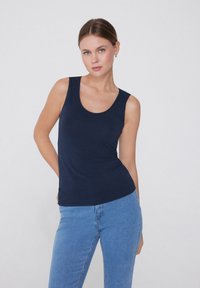 Camiseta sin mangas de color azul marino, hecha de un tejido suave y elástico, con un escote redondeado y un diseño ajustado, combinada con pantalones vaqueros de mezclilla azules.