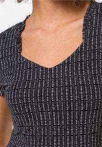 Schwarzes Oberteil mit V-Ausschnitt, ausgestattet mit strukturierten, vertikalen weißen und grauen Mustern. Der Stoff hat einen leichten Stretch und eine weiche Oberfläche.