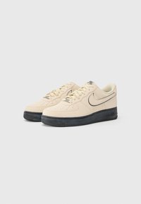 Beige ruskinds sneakers med sort gummisål, rund tå, perforerede detaljer, tykke snøringer og et subtilt swoosh-design.