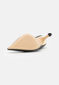 Scarpa nera con punta appuntita e tacco alto, con suola beige texture, caratterizzata da un design elegante e una finitura liscia. Nessun dettaglio di branding visibile.