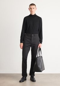 Zwarte aansluitende coltrui met lange mouwen, gecombineerd met zwarte broek en zwarte leren schoudertas. Model draagt zwarte leren schoenen.