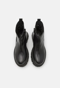 Botas de tobillo negras hechas de cuero suave, con punta redondeada, cremalleras laterales y una suela de goma gruesa con dibujo texturizado.