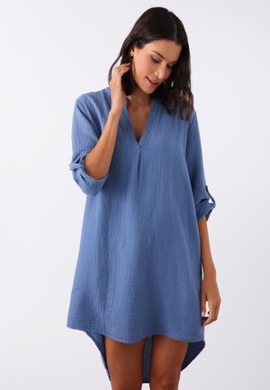 Blaues Baumwollkleid mit V-Ausschnitt und aufgerollten Ärmeln, aus einem strukturierten Stoff mit asymmetrischem Saum, der vorne kürzer ist.