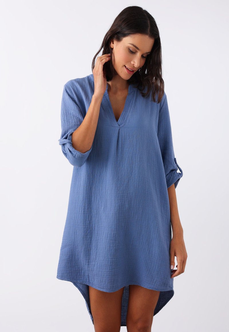 Niebieska sukienka bawełniana z dekoltem w szpic i zwiniętymi rękawami, posiadająca teksturowany materiał i asymetryczny dół krótszy z przodu.
