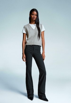 Gray knit sleeveless sweater over a white shirt, paired with black pinstripe flared pants and pointed black shoes. Simple and modern outfit.