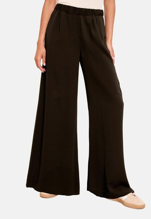 Wide-leg black pants with elastic waistband worn with beige sneakers on a standing person against a plain background.