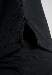 Top deportivo negro con una tela texturizada y ligera. Presenta una abertura lateral y costuras suaves, combinado con un pantalón ajustado negro.