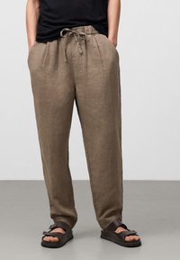 Khaki linnenbroeken met een relaxed fit, een trekkoord in de taille en zijzakken. Gedorven met donkerbruine platte sandalen.