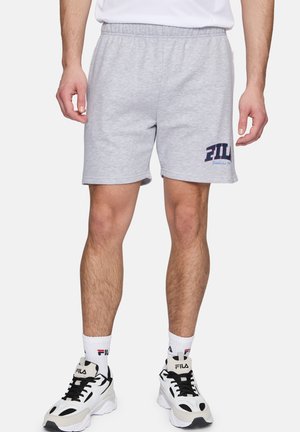 Graue Baumwollshorts mit einem elastischen Bund, versehen mit einem blauen "FIL"-Textlogo am linken Bein. Kombiniert mit schwarz-weißen Turnschuhen.