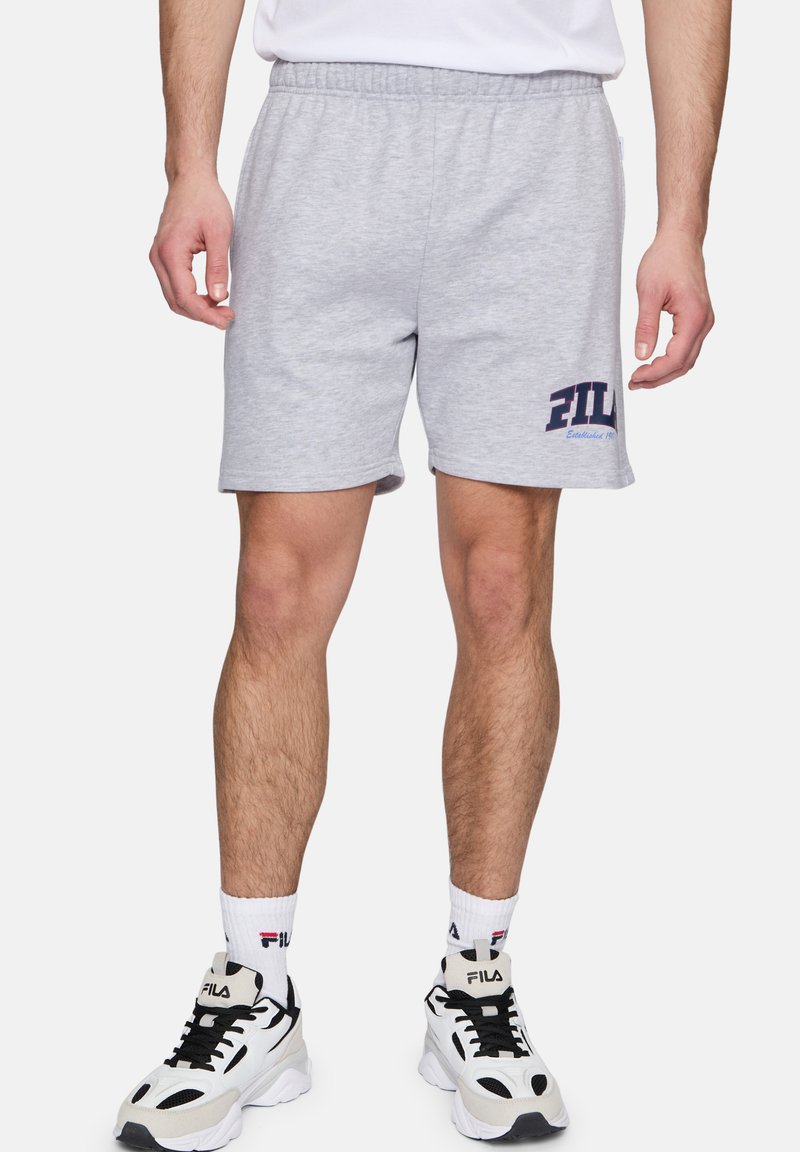 Pantalones cortos de algodón grises con una cinturilla elástica, que presentan un logotipo en texto azul "FIL" en la pierna izquierda. Combinados con zapatillas negras y blancas.