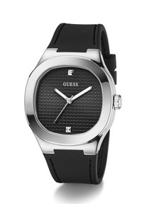 Montre-bracelet GUESS avec cadran texturé noir, boîtier argenté, aiguilles argentées, deux index carrés, et bracelet en silicone noir.