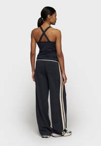 Canotta sportiva nera con spalline incrociate, abbinata a pantaloni neri a vestibilità ampia con strisce laterali beige. Tessuto liscio e traspirante.