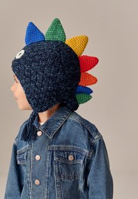 Gehaakte marineblauwe muts met gekleurde stekels (rood, groen, blauw, geel) en ogen. Draag met een denim jack. Heeft gevlochten strikjes.