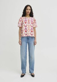 Floral-patterned blouse with short puff sleeves in coral, pink, and purple tones. Paired with loose-fitting light blue jeans and black flats.