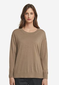 Beige oversized tröja med rund halsringning, långa ärmar och ribbade muddar. Mjuk textur och avslappnad passform; i kombination med mörka byxor.