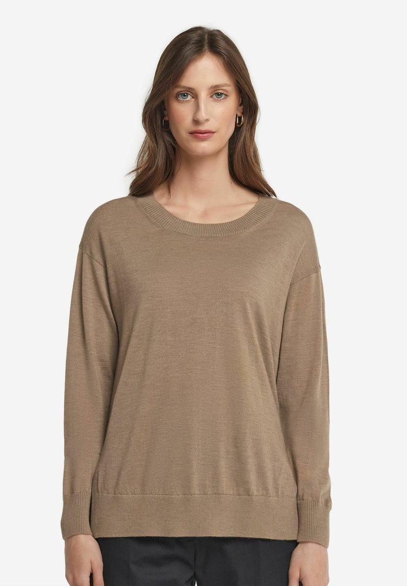 Beige oversized tröja med rund halsringning, långa ärmar och ribbade muddar. Mjuk textur och avslappnad passform; i kombination med mörka byxor.