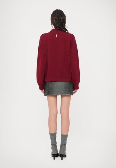 Suéter de malha borgonha com gola redonda e bainha canelada, combinado com mini saia de couro preta e meias cinza caneladas, visto por trás.