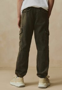 Pantaloni cargo in denim verde scuro, con polsini elasticizzati alla caviglia e numerose tasche. Abbinati a sneaker beige.