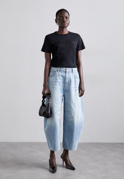 T-shirt preta de manga curta com logótipo em relevo, jeans de perna larga em azul claro, bolsa texturizada preta e sapatos de salto alto transparentes.