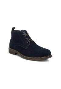 Botines de ante en color navy con cordones marrones, puntera redonda y costuras en contraste. Presentan un tacón bajo de madera y una lengüeta en la parte posterior.